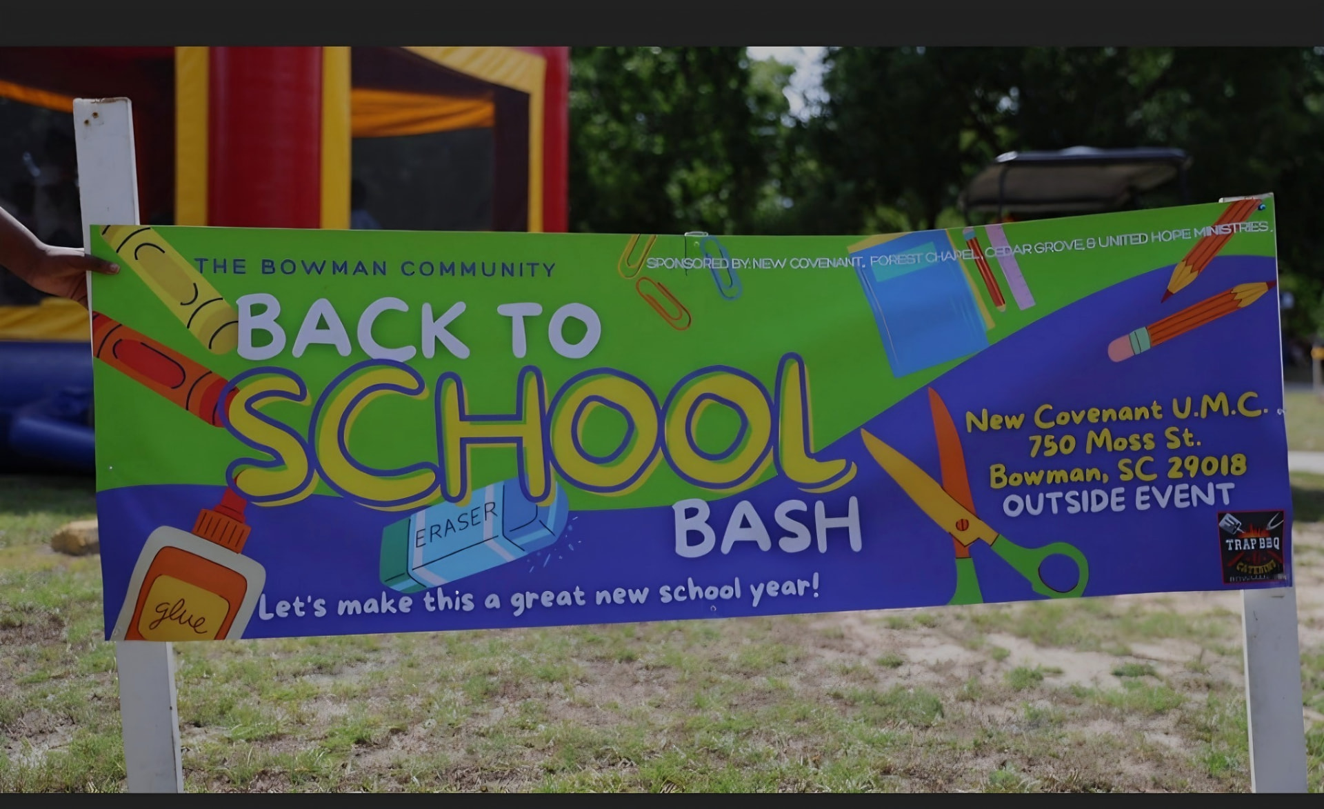 A colorful outdoor banner reading “The Bowman Community Back to School Bash” with school-supply artwork, held upright on a grassy lawn.